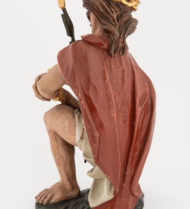 Zdjęcie nr 8: Rzeźba pełnoplastyczna, na podstawie w formie pnia. Chrystus ukazany w pozycji siedzącej, frontalnie, przechylony w prawo, z wysuniętą w bok prawą nogą. Ręce ma ugięte i lekko uniesione, skrzyżowane w nadgarstkach i przewiązane powrozem. Rękami obejmuje trzcinę. Twarz ma trójkątną, o migdałowatych oczach, dużym nosie i pełnych ustach; okoloną krótką brodą oraz silnie skręconymi po bokach głowy włosami, opadającymi na kark. Na głowie ma złoconą koronę cierniową. W partii bioder przewiązany jest białą tkaniną. Na ramiona ma narzucony czerwony płaszcz zawiązany pod szyją. Jego ciało jest szczupłe, ale muskularne. Polichromia ciała naturalistyczna z zaznaczonymi śladami męki. 

