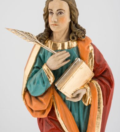 Zdjęcie nr 3: Rzeźba pełna na cokole przedstawiająca św. Jana Ewangelistę. Święty ukazany jest w pozycji stojącej, frontalnie, w kontrapoście, z prawą nogą zgiętą w kolanie i głową skierowaną delikatnie w prawo. Prawą rękę przyciska do piersi, trzymając pióro, lewą przytrzymuje zamkniętą księgę. Ma pociągłą twarz o szeroko otwartych, brązowych oczach, długim nosie i wąskich ustach, okoloną długimi włosami zwijającymi się na końcach w pukle, z przedziałkiem na środku. Ubrany jest w zieloną suknię lamowaną przy krawędziach złotem oraz czerwony, podbity pomarańczowym materiałem płaszcz zarzucony na oba ramiona, układający się w głębokie fałdy. Stopy bose, przy lewej nodze świętego widoczny fragment niewielkiej postaci orła w biało-brązowe cętki, z pomarańczowym dziobem. Polichromia w partiach ciała naturalistyczna, księga i pióro złocone. 