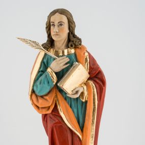 Zdjęcie nr 1: Rzeźba pełna na cokole przedstawiająca św. Jana Ewangelistę. Święty ukazany jest w pozycji stojącej, frontalnie, w kontrapoście, z prawą nogą zgiętą w kolanie i głową skierowaną delikatnie w prawo. Prawą rękę przyciska do piersi, trzymając pióro, lewą przytrzymuje zamkniętą księgę. Ma pociągłą twarz o szeroko otwartych, brązowych oczach, długim nosie i wąskich ustach, okoloną długimi włosami zwijającymi się na końcach w pukle, z przedziałkiem na środku. Ubrany jest w zieloną suknię lamowaną przy krawędziach złotem oraz czerwony, podbity pomarańczowym materiałem płaszcz zarzucony na oba ramiona, układający się w głębokie fałdy. Stopy bose, przy lewej nodze świętego widoczny fragment niewielkiej postaci orła w biało-brązowe cętki, z pomarańczowym dziobem. Polichromia w partiach ciała naturalistyczna, księga i pióro złocone. 