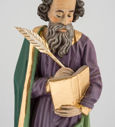 Zdjęcie nr 2: Rzeźba pełna na cokole, przedstawiająca św. Łukasza Ewangelistę. Święty ukazany został w pozycji stojącej, z górną partią ciała skręconą nieznacznie w lewo, w stronę trzymanej w lewej ręce księgi, w której pisze piórem trzymanym w prawej, obie ręce ugięte. Ma pociągłą twarz z przymkniętymi oczami, długim nosem i wąskimi ustami, okoloną wyraźnie zwiniętymi puklami włosów oraz długą, dzielącą się na pasma brodę i wąsy. Święty jest ubrany w przewiązaną w pasie fioletową suknię ze złoconymi lamówkami oraz ciemnozielony płaszcz podbity jasnozielonym materiałem, zarzucony na prawe ramię i otaczający lewe udo, układający się w głębokie fałdy. Stopy bose, przy prawej nodze niewielka, widoczna częściowo postać leżącego woła. Polichromia w partiach ciała naturalistyczna, byk ciemnobrązowy, księga, pióro i rogi byka złocone. 