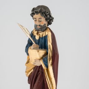 Zdjęcie nr 1: Rzeźba pełna umieszczona na cokole przedstawiająca św. Mateusza Ewangelistę. Święty ukazany jest w pozycji stojącej, frontalnie, w kontrapoście, z lewą nogą zgiętą w kolanie. W prawej ręce trzyma pióro, którym pisze w otwartej księdze przytrzymywanej lewą, głowę ma opuszczoną, wzrok kieruje na wykonywaną czynność. Ma pociągłą twarz o wąskim nosie i małych ustach, okoloną zwiniętymi w wyraźne loki włosami zakrywającymi uszy oraz wąsy i krótką brodę. Ubrany jest w granatową suknię lamowaną przy krawędziach złotem oraz w ciemnobrązowy, podbity beżowym materiałem i lamowany złotem płaszcz zakrywający nogi i plecy, układający się w głębokie fałdy. Stopy bose. Przy prawej nodze świętego widoczna niewielka, klęcząca ze złożonymi rękami postać ludzka o jasnych włosach, okryta złotym płaszczem. Polichromia w partiach ciała naturalistyczna.