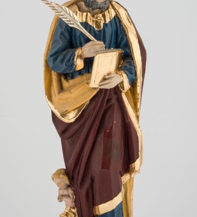 Zdjęcie nr 2: Rzeźba pełna umieszczona na cokole przedstawiająca św. Mateusza Ewangelistę. Święty ukazany jest w pozycji stojącej, frontalnie, w kontrapoście, z lewą nogą zgiętą w kolanie. W prawej ręce trzyma pióro, którym pisze w otwartej księdze przytrzymywanej lewą, głowę ma opuszczoną, wzrok kieruje na wykonywaną czynność. Ma pociągłą twarz o wąskim nosie i małych ustach, okoloną zwiniętymi w wyraźne loki włosami zakrywającymi uszy oraz wąsy i krótką brodę. Ubrany jest w granatową suknię lamowaną przy krawędziach złotem oraz w ciemnobrązowy, podbity beżowym materiałem i lamowany złotem płaszcz zakrywający nogi i plecy, układający się w głębokie fałdy. Stopy bose. Przy prawej nodze świętego widoczna niewielka, klęcząca ze złożonymi rękami postać ludzka o jasnych włosach, okryta złotym płaszczem. Polichromia w partiach ciała naturalistyczna.