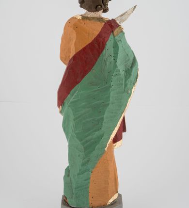 Zdjęcie nr 4: Rzeźba pełna, postać umieszczona na cokole przedstawiająca św. Marka Ewangelistę. Święty ukazany jest w pozycji stojącej, frontalnie, w kontrapoście, z prawą nogą zgiętą w kolanie i głową skierowaną na wprost. Prawą rękę przyciska do piersi, trzymając pióro, lewą przytrzymuje zamkniętą księgę. Święty ma pociągłą twarz o szeroko otwartych, niebieskich oczach, długim nosie i małych ustach, okoloną zwiniętymi w pukle włosami zakrywającymi uszy i formującymi lok nad czołem oraz wąsy i krótką brodę. Ubrany jest w jasnobrązową suknię lamowaną przy krawędziach złotem oraz w zielony, podbity czerwienią i lamowany złotem płaszcz przechodzący przez prawy bark i otaczający lewe biodro, układający się w głębokie fałdy. Stopy bose. Przy lewej nodze świętego widoczny fragment niewielkiej postaci lwa. Polichromia w partiach ciała naturalistyczna. 