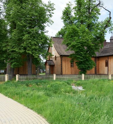 Zdjęcie nr 6: Kościół drewniany o konstrukcji zrębowej, na betonowym podmurowaniu przesłoniętym daszkiem gontowym. Elewacje jednolite, szalowane z listwowaniem, wzmocnione lisicami. Więźba dachowa drewniana, krokwiowa, o systemie więźbowo-zaskrzynieniowym. Kościół orientowany, jednonawowy, nawa na rzucie wydłużonego prostokąta, prezbiterium nieco węższe, zakończone trójbocznie. Do północnej ściany prezbiterium i nawy przylega zakrystia połączona z aneksem na rzucie prostokąta, do nawy od południa przylega duża kaplica na planie prostokąta otwarta do nawy otworem o wykroju prostokąta zamkniętego łukiem odcinkowym. 
Ściany wnętrza podzielone trzema parami pilastrów. Pomiędzy nawą a prezbiterium arkadowy otwór tęczowy z prostą belką. Parapet chóru muzycznego w zachodniej części nawy, oparty na dwóch kolumnach o wielobocznych trzonach. Wnętrze nakryte stropem płaskim, w nawie z zaskrzynieniami podtrzymywanymi przez trzy pary słupów o wielobocznych i kręconych trzonach. Otwory drzwiowe o prostokątnym wykroju zamknięte drzwiami jednoskrzydłowymi w północnej ścianie nawy oraz prezbiterium. Posadzka z płyt kamiennych. 
Elewacja frontowa jednoosiowa, zamknięta trójkątnym szczytem rozszerzającym się ku dołowi. Na osi ganek oparty na czterech słupach, nakryty dwuspadowym daszkiem gontowym, wejście do kościoła z dwuskrzydłowymi drzwiami. W partii szczytu dwa okna w formie stojącego prostokąta zamkniętego łukiem półkolistym. W elewacji południowej cztery otwory okienne w formie stojącego prostokąta zamkniętego łukiem półkolistym, dwa w nawie i dwa w prezbiterium oraz dwa analogiczne okna na zachodniej i wschodniej ścianie kaplicy. Elewacja północna z dwoma otworami okiennymi w formie stojącego prostokąta zamkniętego łukiem półkolistym, trzema oknami i wejściem do zakrystii i aneksu. Kościół nakryty wspólnym dachem o jednej kalenicy nad prezbiterium i nawą, gontowym, dwuspadowym, z przedłużoną połacią przekrywającą zaskrzynienia. W jednej trzeciej długości dachu nad nawą od strony prezbiterium wznosi się ponad kalenicą wieżyczka na sygnaturkę, na ośmiobocznym obitym blachą trzonie, z latarnią zwieńczoną niewielkim cebulastym hełmem. Kaplica boczna nakryta kopułą krytą gontem, z latarnią. Nad zakrystią i aneksem dach jednospadowy.
 
