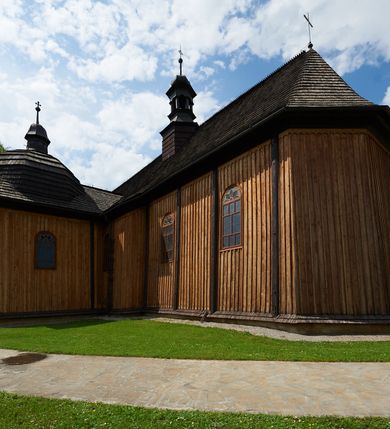 Zdjęcie nr 7: Kościół drewniany o konstrukcji zrębowej, na betonowym podmurowaniu przesłoniętym daszkiem gontowym. Elewacje jednolite, szalowane z listwowaniem, wzmocnione lisicami. Więźba dachowa drewniana, krokwiowa, o systemie więźbowo-zaskrzynieniowym. Kościół orientowany, jednonawowy, nawa na rzucie wydłużonego prostokąta, prezbiterium nieco węższe, zakończone trójbocznie. Do północnej ściany prezbiterium i nawy przylega zakrystia połączona z aneksem na rzucie prostokąta, do nawy od południa przylega duża kaplica na planie prostokąta otwarta do nawy otworem o wykroju prostokąta zamkniętego łukiem odcinkowym. 
Ściany wnętrza podzielone trzema parami pilastrów. Pomiędzy nawą a prezbiterium arkadowy otwór tęczowy z prostą belką. Parapet chóru muzycznego w zachodniej części nawy, oparty na dwóch kolumnach o wielobocznych trzonach. Wnętrze nakryte stropem płaskim, w nawie z zaskrzynieniami podtrzymywanymi przez trzy pary słupów o wielobocznych i kręconych trzonach. Otwory drzwiowe o prostokątnym wykroju zamknięte drzwiami jednoskrzydłowymi w północnej ścianie nawy oraz prezbiterium. Posadzka z płyt kamiennych. 
Elewacja frontowa jednoosiowa, zamknięta trójkątnym szczytem rozszerzającym się ku dołowi. Na osi ganek oparty na czterech słupach, nakryty dwuspadowym daszkiem gontowym, wejście do kościoła z dwuskrzydłowymi drzwiami. W partii szczytu dwa okna w formie stojącego prostokąta zamkniętego łukiem półkolistym. W elewacji południowej cztery otwory okienne w formie stojącego prostokąta zamkniętego łukiem półkolistym, dwa w nawie i dwa w prezbiterium oraz dwa analogiczne okna na zachodniej i wschodniej ścianie kaplicy. Elewacja północna z dwoma otworami okiennymi w formie stojącego prostokąta zamkniętego łukiem półkolistym, trzema oknami i wejściem do zakrystii i aneksu. Kościół nakryty wspólnym dachem o jednej kalenicy nad prezbiterium i nawą, gontowym, dwuspadowym, z przedłużoną połacią przekrywającą zaskrzynienia. W jednej trzeciej długości dachu nad nawą od strony prezbiterium wznosi się ponad kalenicą wieżyczka na sygnaturkę, na ośmiobocznym obitym blachą trzonie, z latarnią zwieńczoną niewielkim cebulastym hełmem. Kaplica boczna nakryta kopułą krytą gontem, z latarnią. Nad zakrystią i aneksem dach jednospadowy.
 
