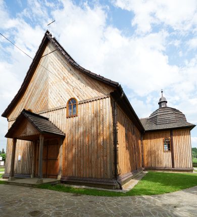 Zdjęcie nr 1: Kościół drewniany o konstrukcji zrębowej, na betonowym podmurowaniu przesłoniętym daszkiem gontowym. Elewacje jednolite, szalowane z listwowaniem, wzmocnione lisicami. Więźba dachowa drewniana, krokwiowa, o systemie więźbowo-zaskrzynieniowym. Kościół orientowany, jednonawowy, nawa na rzucie wydłużonego prostokąta, prezbiterium nieco węższe, zakończone trójbocznie. Do północnej ściany prezbiterium i nawy przylega zakrystia połączona z aneksem na rzucie prostokąta, do nawy od południa przylega duża kaplica na planie prostokąta otwarta do nawy otworem o wykroju prostokąta zamkniętego łukiem odcinkowym. 
Ściany wnętrza podzielone trzema parami pilastrów. Pomiędzy nawą a prezbiterium arkadowy otwór tęczowy z prostą belką. Parapet chóru muzycznego w zachodniej części nawy, oparty na dwóch kolumnach o wielobocznych trzonach. Wnętrze nakryte stropem płaskim, w nawie z zaskrzynieniami podtrzymywanymi przez trzy pary słupów o wielobocznych i kręconych trzonach. Otwory drzwiowe o prostokątnym wykroju zamknięte drzwiami jednoskrzydłowymi w północnej ścianie nawy oraz prezbiterium. Posadzka z płyt kamiennych. 
Elewacja frontowa jednoosiowa, zamknięta trójkątnym szczytem rozszerzającym się ku dołowi. Na osi ganek oparty na czterech słupach, nakryty dwuspadowym daszkiem gontowym, wejście do kościoła z dwuskrzydłowymi drzwiami. W partii szczytu dwa okna w formie stojącego prostokąta zamkniętego łukiem półkolistym. W elewacji południowej cztery otwory okienne w formie stojącego prostokąta zamkniętego łukiem półkolistym, dwa w nawie i dwa w prezbiterium oraz dwa analogiczne okna na zachodniej i wschodniej ścianie kaplicy. Elewacja północna z dwoma otworami okiennymi w formie stojącego prostokąta zamkniętego łukiem półkolistym, trzema oknami i wejściem do zakrystii i aneksu. Kościół nakryty wspólnym dachem o jednej kalenicy nad prezbiterium i nawą, gontowym, dwuspadowym, z przedłużoną połacią przekrywającą zaskrzynienia. W jednej trzeciej długości dachu nad nawą od strony prezbiterium wznosi się ponad kalenicą wieżyczka na sygnaturkę, na ośmiobocznym obitym blachą trzonie, z latarnią zwieńczoną niewielkim cebulastym hełmem. Kaplica boczna nakryta kopułą krytą gontem, z latarnią. Nad zakrystią i aneksem dach jednospadowy.
 
