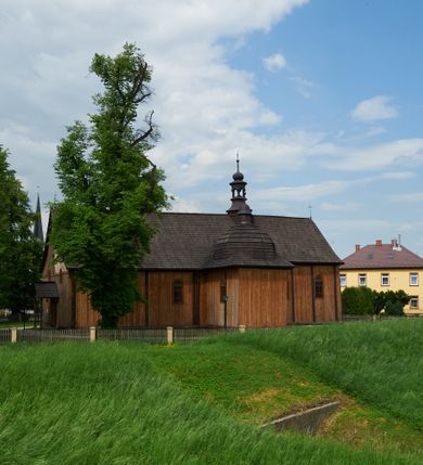 Zdjęcie nr 5: Kościół drewniany o konstrukcji zrębowej, na betonowym podmurowaniu przesłoniętym daszkiem gontowym. Elewacje jednolite, szalowane z listwowaniem, wzmocnione lisicami. Więźba dachowa drewniana, krokwiowa, o systemie więźbowo-zaskrzynieniowym. Kościół orientowany, jednonawowy, nawa na rzucie wydłużonego prostokąta, prezbiterium nieco węższe, zakończone trójbocznie. Do północnej ściany prezbiterium i nawy przylega zakrystia połączona z aneksem na rzucie prostokąta, do nawy od południa przylega duża kaplica na planie prostokąta otwarta do nawy otworem o wykroju prostokąta zamkniętego łukiem odcinkowym. 
Ściany wnętrza podzielone trzema parami pilastrów. Pomiędzy nawą a prezbiterium arkadowy otwór tęczowy z prostą belką. Parapet chóru muzycznego w zachodniej części nawy, oparty na dwóch kolumnach o wielobocznych trzonach. Wnętrze nakryte stropem płaskim, w nawie z zaskrzynieniami podtrzymywanymi przez trzy pary słupów o wielobocznych i kręconych trzonach. Otwory drzwiowe o prostokątnym wykroju zamknięte drzwiami jednoskrzydłowymi w północnej ścianie nawy oraz prezbiterium. Posadzka z płyt kamiennych. 
Elewacja frontowa jednoosiowa, zamknięta trójkątnym szczytem rozszerzającym się ku dołowi. Na osi ganek oparty na czterech słupach, nakryty dwuspadowym daszkiem gontowym, wejście do kościoła z dwuskrzydłowymi drzwiami. W partii szczytu dwa okna w formie stojącego prostokąta zamkniętego łukiem półkolistym. W elewacji południowej cztery otwory okienne w formie stojącego prostokąta zamkniętego łukiem półkolistym, dwa w nawie i dwa w prezbiterium oraz dwa analogiczne okna na zachodniej i wschodniej ścianie kaplicy. Elewacja północna z dwoma otworami okiennymi w formie stojącego prostokąta zamkniętego łukiem półkolistym, trzema oknami i wejściem do zakrystii i aneksu. Kościół nakryty wspólnym dachem o jednej kalenicy nad prezbiterium i nawą, gontowym, dwuspadowym, z przedłużoną połacią przekrywającą zaskrzynienia. W jednej trzeciej długości dachu nad nawą od strony prezbiterium wznosi się ponad kalenicą wieżyczka na sygnaturkę, na ośmiobocznym obitym blachą trzonie, z latarnią zwieńczoną niewielkim cebulastym hełmem. Kaplica boczna nakryta kopułą krytą gontem, z latarnią. Nad zakrystią i aneksem dach jednospadowy.
 
