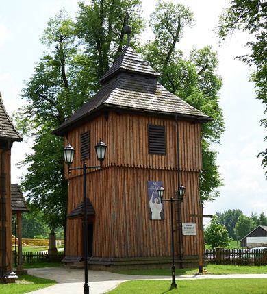 Zdjęcie nr 1: Dzwonnica drewniana, konstrukcji słupowej, ściany, szalowane z listwowaniem, więźba dachowa drewniana. Założona na planie kwadratu, na betonowym podmurowaniu, przesłoniętym okapowym daszkiem gontowym. Ściany zwężające się ku górze, z izbicą. Dach gontowy, czterospadowy, łamany, zakończony metalowym szpikulcem z kulą i krzyżem. Otwór drzwiowy w ścianie wschodniej o wykroju stojącego prostokąta zamknięty drzwiami jednoskrzydłowymi, nakryty trójspadowym daszkiem gontowym. Otwory głosowe w formie stojącego prostokąta, po jednym na każdej ścianie w partii izbicy. 
