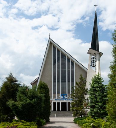 Zdjęcie nr 1: Świątynia trójnawowa, ośmioprzęsłowa o konstrukcji żelbetowej, tynkowana. Prezbiterium zamknięte prostą ścianą, umieszczone na kilkustopniowym podwyższeniu. Prostokątna zakrystia od strony wschodniej oraz prostokątna kaplica od strony zachodniej. Nawy, z których środkowa wyższa i szersza od bocznych wydzielone smukłymi filarami na rzucie prostokąta. Nakryte ekspresyjnym, żelbetowym stropem o rzeźbiarskiej formie. Chór muzyczny od strony południowej o konstrukcji żelbetowej z prostym parapetem zamkniętym od góry drewnianą poręczą. Fasada dwukondygnacyjna z umieszczonym w przyziemiu pięcioosiowym wejściem w formie prostokątnych otworów drzwiowych dostępnych wysokimi schodami. Otwory drzwiowe wydzielone żelbetowymi lizenami, podziały kontynuowane także w drugiej kondygnacji, gdzie w miejsce otworów drzwiowych wysokie, prostokątne okna. Elewacja zamknięta ścianą szczytową w kształcie trójkąta o nierównych bokach i zwieńczona prostym krzyżem. Od zachodu do elewacji dostawiona wieża dzwonna na rzucie trójkąta zwężającego się ku górze i nakryta strzelistym, ostrosłupowym hełmem zwieńczonym krzyżem. Elewacje boczne ośmioosiowe, artykułowane lizenami. W czterech pierwszych osiach od południa i na szerokości prezbiterium po dwa wysokie i prostokątne okna, w pozostałych pojedyncze okna i trójkątne szczyty. Od wschodu dach kryty blachą, dwuspadowy o nierównych połaciach; nad nawą boczną od strony wschodniej jednopołaciowy. Niewielka wieżyczka na sygnaturkę na kalenicy dachu od strony północnej.