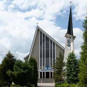 Zdjęcie nr 1: Świątynia trójnawowa, ośmioprzęsłowa o konstrukcji żelbetowej, tynkowana. Prezbiterium zamknięte prostą ścianą, umieszczone na kilkustopniowym podwyższeniu. Prostokątna zakrystia od strony wschodniej oraz prostokątna kaplica od strony zachodniej. Nawy, z których środkowa wyższa i szersza od bocznych wydzielone smukłymi filarami na rzucie prostokąta. Nakryte ekspresyjnym, żelbetowym stropem o rzeźbiarskiej formie. Chór muzyczny od strony południowej o konstrukcji żelbetowej z prostym parapetem zamkniętym od góry drewnianą poręczą. Fasada dwukondygnacyjna z umieszczonym w przyziemiu pięcioosiowym wejściem w formie prostokątnych otworów drzwiowych dostępnych wysokimi schodami. Otwory drzwiowe wydzielone żelbetowymi lizenami, podziały kontynuowane także w drugiej kondygnacji, gdzie w miejsce otworów drzwiowych wysokie, prostokątne okna. Elewacja zamknięta ścianą szczytową w kształcie trójkąta o nierównych bokach i zwieńczona prostym krzyżem. Od zachodu do elewacji dostawiona wieża dzwonna na rzucie trójkąta zwężającego się ku górze i nakryta strzelistym, ostrosłupowym hełmem zwieńczonym krzyżem. Elewacje boczne ośmioosiowe, artykułowane lizenami. W czterech pierwszych osiach od południa i na szerokości prezbiterium po dwa wysokie i prostokątne okna, w pozostałych pojedyncze okna i trójkątne szczyty. Od wschodu dach kryty blachą, dwuspadowy o nierównych połaciach; nad nawą boczną od strony wschodniej jednopołaciowy. Niewielka wieżyczka na sygnaturkę na kalenicy dachu od strony północnej.