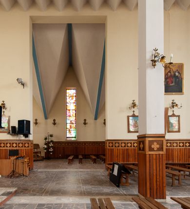 Zdjęcie nr 9: Świątynia trójnawowa, ośmioprzęsłowa o konstrukcji żelbetowej, tynkowana. Prezbiterium zamknięte prostą ścianą, umieszczone na kilkustopniowym podwyższeniu. Prostokątna zakrystia od strony wschodniej oraz prostokątna kaplica od strony zachodniej. Nawy, z których środkowa wyższa i szersza od bocznych wydzielone smukłymi filarami na rzucie prostokąta. Nakryte ekspresyjnym, żelbetowym stropem o rzeźbiarskiej formie. Chór muzyczny od strony południowej o konstrukcji żelbetowej z prostym parapetem zamkniętym od góry drewnianą poręczą. Fasada dwukondygnacyjna z umieszczonym w przyziemiu pięcioosiowym wejściem w formie prostokątnych otworów drzwiowych dostępnych wysokimi schodami. Otwory drzwiowe wydzielone żelbetowymi lizenami, podziały kontynuowane także w drugiej kondygnacji, gdzie w miejsce otworów drzwiowych wysokie, prostokątne okna. Elewacja zamknięta ścianą szczytową w kształcie trójkąta o nierównych bokach i zwieńczona prostym krzyżem. Od zachodu do elewacji dostawiona wieża dzwonna na rzucie trójkąta zwężającego się ku górze i nakryta strzelistym, ostrosłupowym hełmem zwieńczonym krzyżem. Elewacje boczne ośmioosiowe, artykułowane lizenami. W czterech pierwszych osiach od południa i na szerokości prezbiterium po dwa wysokie i prostokątne okna, w pozostałych pojedyncze okna i trójkątne szczyty. Od wschodu dach kryty blachą, dwuspadowy o nierównych połaciach; nad nawą boczną od strony wschodniej jednopołaciowy. Niewielka wieżyczka na sygnaturkę na kalenicy dachu od strony północnej.