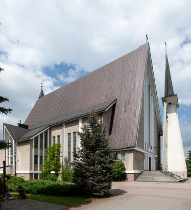 Zdjęcie nr 3: Świątynia trójnawowa, ośmioprzęsłowa o konstrukcji żelbetowej, tynkowana. Prezbiterium zamknięte prostą ścianą, umieszczone na kilkustopniowym podwyższeniu. Prostokątna zakrystia od strony wschodniej oraz prostokątna kaplica od strony zachodniej. Nawy, z których środkowa wyższa i szersza od bocznych wydzielone smukłymi filarami na rzucie prostokąta. Nakryte ekspresyjnym, żelbetowym stropem o rzeźbiarskiej formie. Chór muzyczny od strony południowej o konstrukcji żelbetowej z prostym parapetem zamkniętym od góry drewnianą poręczą. Fasada dwukondygnacyjna z umieszczonym w przyziemiu pięcioosiowym wejściem w formie prostokątnych otworów drzwiowych dostępnych wysokimi schodami. Otwory drzwiowe wydzielone żelbetowymi lizenami, podziały kontynuowane także w drugiej kondygnacji, gdzie w miejsce otworów drzwiowych wysokie, prostokątne okna. Elewacja zamknięta ścianą szczytową w kształcie trójkąta o nierównych bokach i zwieńczona prostym krzyżem. Od zachodu do elewacji dostawiona wieża dzwonna na rzucie trójkąta zwężającego się ku górze i nakryta strzelistym, ostrosłupowym hełmem zwieńczonym krzyżem. Elewacje boczne ośmioosiowe, artykułowane lizenami. W czterech pierwszych osiach od południa i na szerokości prezbiterium po dwa wysokie i prostokątne okna, w pozostałych pojedyncze okna i trójkątne szczyty. Od wschodu dach kryty blachą, dwuspadowy o nierównych połaciach; nad nawą boczną od strony wschodniej jednopołaciowy. Niewielka wieżyczka na sygnaturkę na kalenicy dachu od strony północnej.