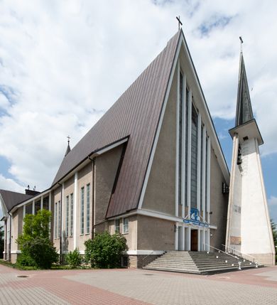 Zdjęcie nr 2: Świątynia trójnawowa, ośmioprzęsłowa o konstrukcji żelbetowej, tynkowana. Prezbiterium zamknięte prostą ścianą, umieszczone na kilkustopniowym podwyższeniu. Prostokątna zakrystia od strony wschodniej oraz prostokątna kaplica od strony zachodniej. Nawy, z których środkowa wyższa i szersza od bocznych wydzielone smukłymi filarami na rzucie prostokąta. Nakryte ekspresyjnym, żelbetowym stropem o rzeźbiarskiej formie. Chór muzyczny od strony południowej o konstrukcji żelbetowej z prostym parapetem zamkniętym od góry drewnianą poręczą. Fasada dwukondygnacyjna z umieszczonym w przyziemiu pięcioosiowym wejściem w formie prostokątnych otworów drzwiowych dostępnych wysokimi schodami. Otwory drzwiowe wydzielone żelbetowymi lizenami, podziały kontynuowane także w drugiej kondygnacji, gdzie w miejsce otworów drzwiowych wysokie, prostokątne okna. Elewacja zamknięta ścianą szczytową w kształcie trójkąta o nierównych bokach i zwieńczona prostym krzyżem. Od zachodu do elewacji dostawiona wieża dzwonna na rzucie trójkąta zwężającego się ku górze i nakryta strzelistym, ostrosłupowym hełmem zwieńczonym krzyżem. Elewacje boczne ośmioosiowe, artykułowane lizenami. W czterech pierwszych osiach od południa i na szerokości prezbiterium po dwa wysokie i prostokątne okna, w pozostałych pojedyncze okna i trójkątne szczyty. Od wschodu dach kryty blachą, dwuspadowy o nierównych połaciach; nad nawą boczną od strony wschodniej jednopołaciowy. Niewielka wieżyczka na sygnaturkę na kalenicy dachu od strony północnej.