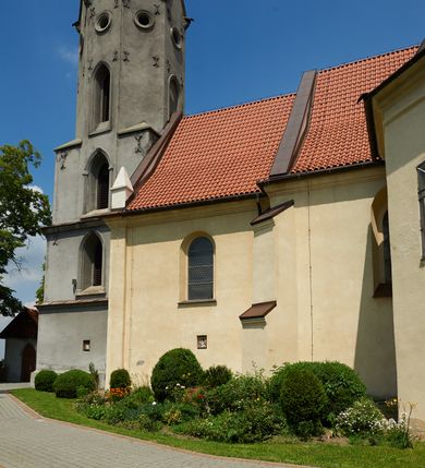 Zdjęcie nr 13: Kościół murowany z cegły i kamienia, tynkowany. Detal architektoniczny kamienny i rzeźbiony w tynku. Więźba dachowa drewniana, krokwiowa. Świątynia orientowana, jednonawowa, nawa na rzucie wydłużonego prostokąta, prezbiterium nieco węższe, zakończone wielobocznie, z wieżą na planie kwadratu. Do prezbiterium od północy przylega zakrystia z przedsionkiem i kruchtą na planie zbliżonym do prostokąta, do nawy od południa przybudowana kaplica na rzucie ośmioboku oraz od północy kruchta na planie kwadratu. Całość oszkarpowana. Wnętrze nakryte drewnianymi stropami i sufitami z wyprawą tynkową i polichromią. Pomiędzy nawą a prezbiterium półkolisty otwór tęczowy. Parapet chóru muzycznego w zachodniej części nawy, podparty na dwóch kolumnach. Otwory drzwiowe o wykroju prostokątnym, ostrołukowym i prostokątnym zamkniętym łukiem segmentowym. Drzwi drewniane obite listwami i płycinowe. Okna w formie stojącego prostokąta zamkniętego łukiem półkolistym, w wieży zamknięte łukiem ostrym, w metalowej oprawie, witrażowe. Posadzka z płyt ceramicznych. Elewacje opracowane jednolicie, tynkowane, zakończone gzymsem podokapowym, opięte dwuuskokowymi szkarpami. Elewacja zachodnia wieżowa, jednoosiowa, czterokondygnacyjna, z wydzielonym cokołem. Kondygnacje wydzielone gzymsami kordonowymi, ostatnia na planie ośmioboku. Na osi ostrołukowy portal z profilowanym obramieniem w tynku. Drzwi drewniane dwuskrzydłowe, obite listwami, z ostrołukowym naświetlem. Nad portalem owalna tablica fundacyjna z napisem „WIEŻA TA WYBUDOWANA / NA CZEŚĆ / MATKI BOSKIEJ / R(OKU) P(AŃSKIEGO) 1888”. Na froncie wieży, na osi, dwa ostrołukowe okna, na ścianach bocznych po trzy ostrołukowe okna, w najwyższej partii rząd okulusów. Wieża zakończona ośmioma trójkątnymi szczytami i ostrosłupowym hełmem z metalową koroną. Elewacje boczne przeprute oknami, po dwa w nawie i prezbiterium, alternowanymi szkarpami. W kaplicy i w zakrystii po dwa okna. Elewacja wschodnia pozbawiona okien. Kruchta północna przybudowana do korpusu, od frontu ujęta stylizowanymi półkolumnami dźwigającymi wklęsło-wypukły szczyt. W zewnętrzne ściany kościoła wmurowane współczesne, ceramiczne stacje drogi krzyżowej. Dachy dwuspadowe, kryte dachówką ceramiczną. Wyższy nad nawą, niższy nad prezbiterium. W połowie długości dachu, nad nawą, wieżyczka na sygnaturkę z latarnią, zwieńczona ostrosłupowym hełmem. Nad zakrystią ceramiczny dach pulpitowy, nad kruchtą dwuspadowy, nad kaplicą ostrosłupowy, kryty blachą. 