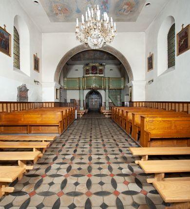 Zdjęcie nr 14: Kościół murowany z cegły i kamienia, tynkowany. Detal architektoniczny kamienny i rzeźbiony w tynku. Więźba dachowa drewniana, krokwiowa. Świątynia orientowana, jednonawowa, nawa na rzucie wydłużonego prostokąta, prezbiterium nieco węższe, zakończone wielobocznie, z wieżą na planie kwadratu. Do prezbiterium od północy przylega zakrystia z przedsionkiem i kruchtą na planie zbliżonym do prostokąta, do nawy od południa przybudowana kaplica na rzucie ośmioboku oraz od północy kruchta na planie kwadratu. Całość oszkarpowana. Wnętrze nakryte drewnianymi stropami i sufitami z wyprawą tynkową i polichromią. Pomiędzy nawą a prezbiterium półkolisty otwór tęczowy. Parapet chóru muzycznego w zachodniej części nawy, podparty na dwóch kolumnach. Otwory drzwiowe o wykroju prostokątnym, ostrołukowym i prostokątnym zamkniętym łukiem segmentowym. Drzwi drewniane obite listwami i płycinowe. Okna w formie stojącego prostokąta zamkniętego łukiem półkolistym, w wieży zamknięte łukiem ostrym, w metalowej oprawie, witrażowe. Posadzka z płyt ceramicznych. Elewacje opracowane jednolicie, tynkowane, zakończone gzymsem podokapowym, opięte dwuuskokowymi szkarpami. Elewacja zachodnia wieżowa, jednoosiowa, czterokondygnacyjna, z wydzielonym cokołem. Kondygnacje wydzielone gzymsami kordonowymi, ostatnia na planie ośmioboku. Na osi ostrołukowy portal z profilowanym obramieniem w tynku. Drzwi drewniane dwuskrzydłowe, obite listwami, z ostrołukowym naświetlem. Nad portalem owalna tablica fundacyjna z napisem „WIEŻA TA WYBUDOWANA / NA CZEŚĆ / MATKI BOSKIEJ / R(OKU) P(AŃSKIEGO) 1888”. Na froncie wieży, na osi, dwa ostrołukowe okna, na ścianach bocznych po trzy ostrołukowe okna, w najwyższej partii rząd okulusów. Wieża zakończona ośmioma trójkątnymi szczytami i ostrosłupowym hełmem z metalową koroną. Elewacje boczne przeprute oknami, po dwa w nawie i prezbiterium, alternowanymi szkarpami. W kaplicy i w zakrystii po dwa okna. Elewacja wschodnia pozbawiona okien. Kruchta północna przybudowana do korpusu, od frontu ujęta stylizowanymi półkolumnami dźwigającymi wklęsło-wypukły szczyt. W zewnętrzne ściany kościoła wmurowane współczesne, ceramiczne stacje drogi krzyżowej. Dachy dwuspadowe, kryte dachówką ceramiczną. Wyższy nad nawą, niższy nad prezbiterium. W połowie długości dachu, nad nawą, wieżyczka na sygnaturkę z latarnią, zwieńczona ostrosłupowym hełmem. Nad zakrystią ceramiczny dach pulpitowy, nad kruchtą dwuspadowy, nad kaplicą ostrosłupowy, kryty blachą. 