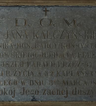 Zdjęcie nr 1: Epitafium w kształcie leżącego prostokąta w profilowanej kamiennej ramie z inskrypcją: „D(EO) O(PTIMO) M(AXIMO) / Ś(WIĘTEJ) P(AMIĘCI) KS(IĘDZA) JANA KALCZYŃSKIEGO / KANONIKA HON(OROWEGO), RADCY KONSYSTORZA / KRAKOWSKIEGO, JUBILATA, PLEBANA / TUTEJSZEJ PARAFII PRZEZ 47 LAT, / W 81 R(OKU) ŻYCIA, A 52 KAPŁAŃSTWA, / ZMARŁEGO W DNIU 3 GO MARCA 1883 R(OKU) / Pokój Jego zacnej duszy!” Nad inskrypcją krzyż. 
