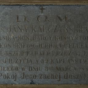 Zdjęcie nr 1: Epitafium w kształcie leżącego prostokąta w profilowanej kamiennej ramie z inskrypcją: „D(EO) O(PTIMO) M(AXIMO) / Ś(WIĘTEJ) P(AMIĘCI) KS(IĘDZA) JANA KALCZYŃSKIEGO / KANONIKA HON(OROWEGO), RADCY KONSYSTORZA / KRAKOWSKIEGO, JUBILATA, PLEBANA / TUTEJSZEJ PARAFII PRZEZ 47 LAT, / W 81 R(OKU) ŻYCIA, A 52 KAPŁAŃSTWA, / ZMARŁEGO W DNIU 3 GO MARCA 1883 R(OKU) / Pokój Jego zacnej duszy!” Nad inskrypcją krzyż. 

