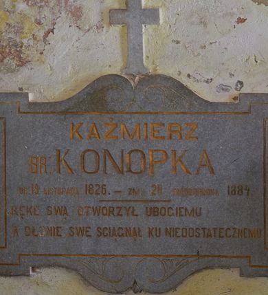 Zdjęcie nr 1: Epitafium w formie leżącego prostokąta, z uszakami, ujęte od góry i dołu wolutami, zwieńczone prostym krzyżem. W polu inskrypcja „KAŻMIERZ / BR: KONOPKA / UR(ODZONY) 19 LISTOPADA 1826. – ZM(ARŁY) 28 PAŹDZIERNIKA 1884. / RĘKE SWĄ OTWORZYŁ UBOGIEMU / A DŁONIE SWE ŚCIĄGNĄŁ KU NIEDOSTATECZNEMU”. 