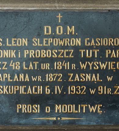 Zdjęcie nr 1: Epitafium w kształcie leżącego prostokąta w profilowanej kamiennej ramie. W polu inskrypcja „D(EO) O(PTIMO) M(AXIMO) / Ś(WIĘTEJ) P(AMIĘCI) KS(IĄDZ) LEON SLEPOWRON GĄSIOROWSKI / KANONIK i PROBOSZCZ TUT(EJSZEJ) PARAFJI / PRZEZ 48 LAT. UR(ODZONY) 1841 R(OKU) WYŚWIĘCONY / NA KAPŁANA W R(OKU) 1872. ZASNĄŁ W PANU / W BISKUPICACH 6. IV. 1932 W 91 R(OKU) ŻYCIA / PROSI O MODLITWĘ”.

