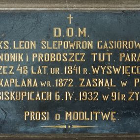 Zdjęcie nr 1: Epitafium w kształcie leżącego prostokąta w profilowanej kamiennej ramie. W polu inskrypcja „D(EO) O(PTIMO) M(AXIMO) / Ś(WIĘTEJ) P(AMIĘCI) KS(IĄDZ) LEON SLEPOWRON GĄSIOROWSKI / KANONIK i PROBOSZCZ TUT(EJSZEJ) PARAFJI / PRZEZ 48 LAT. UR(ODZONY) 1841 R(OKU) WYŚWIĘCONY / NA KAPŁANA W R(OKU) 1872. ZASNĄŁ W PANU / W BISKUPICACH 6. IV. 1932 W 91 R(OKU) ŻYCIA / PROSI O MODLITWĘ”.

