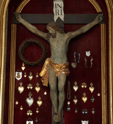 Zdjęcie nr 1: Rzeźba Chrystusa umarłego przybita do prostego krzyża trzema gwoździami. Ciało w lekkim zwisie o szeroko rozłożonych ramionach, układających się w delikatny łuk, głowa opadająca na prawy bark, nogi ugięte w kolanach, stopy skrzyżowane w układzie prawa na lewą. Chrystus ma pociągłą twarz, o migdałowatych, zamkniętych oczach, wąskim nosie i małych, rozchylonych ustach. Twarz okolona krótką, falowaną i rozdwajającą się w dwa pukle brodą oraz falowanymi włosami opadającymi na prawe ramię i kark. Ciało szczupłe, o delikatnym zarysowanym modelunku mięśni klatki piersiowej oraz ramion i nóg. Biodra przewiązane krótkim perizonium, zawiązanym na prawym boku. Ciało figury polichromowane naturalistycznie, włosy w kolorze brązowym, perizonium złocone. Na pionowej belce krzyża tabliczka z napisem „IN / RI”.

