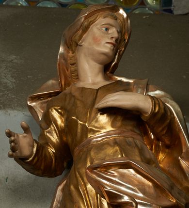 Zdjęcie nr 3: Rzeźba drążona z tyłu, ustawiona na niskiej podstawie. Figura zwrócona jest frontalnie, z głową skierowaną w lewo, w kontrapoście, o odchylonej i esowato wygiętej sylwetce. Twarz ma szczupłą, o migdałowatych, głęboko osadzonych oczach, prostym nosie, wąskich ustach, z uwypukloną brodą, okoloną jasnymi, falowanymi włosami ukrytymi pod welonem. Święta ubrana jest w przylegającą do ciała złoconą tunikę przepasaną w talii, na lewe ramię ma narzucony płaszcz, opadający po bokach postaci z fragmentem tkaniny zarzuconym na lewą nogę, na głowie ma welon, rozwiany na plecy. Ciało polichromowane naturalistycznie.
