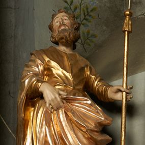 Zdjęcie nr 1: Rzeźba drążona z tyłu, ustawiona na niskiej podstawie. Figura zwrócona jest frontalnie, z uniesioną głową skierowaną w prawo, odchylona, w kontrapoście. W lewej odchylonej od ciała ręce trzyma włócznię, prawą podtrzymuje z przodu połę płaszcza. Twarz ma szczupłą, o głęboko osadzonych oczach skierowanych do góry, lekko garbatym nosie i wąskich rozchylonych ustach, okoloną gęstą, silnie skręconą w dwa grube pukle brodą. Włosy ma brązowe, krótkie, kręcone. Joachim ubrany jest w złoconą tunikę, przepasaną w talii oraz złocony płaszcz zarzucony na prawe ramię, otaczający postać, z połą tkaniny podtrzymywaną z przodu prawą ręką. Polichromia ciała naturalistyczna. 