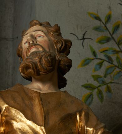 Zdjęcie nr 4: Rzeźba drążona z tyłu, ustawiona na niskiej podstawie. Figura zwrócona jest frontalnie, z uniesioną głową skierowaną w prawo, odchylona, w kontrapoście. W lewej odchylonej od ciała ręce trzyma włócznię, prawą podtrzymuje z przodu połę płaszcza. Twarz ma szczupłą, o głęboko osadzonych oczach skierowanych do góry, lekko garbatym nosie i wąskich rozchylonych ustach, okoloną gęstą, silnie skręconą w dwa grube pukle brodą. Włosy ma brązowe, krótkie, kręcone. Joachim ubrany jest w złoconą tunikę, przepasaną w talii oraz złocony płaszcz zarzucony na prawe ramię, otaczający postać, z połą tkaniny podtrzymywaną z przodu prawą ręką. Polichromia ciała naturalistyczna. 