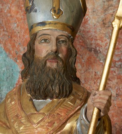 Zdjęcie nr 9: Rzeźba jest drążona i ścięta z tyłu, ustawiona na niskiej podstawie na planie kwadratu. Święty zwrócony jest frontalnie, z głową skierowaną delikatnie w lewo, w kontrapoście. Obie ręce ma ugięte i rozłożone na boki, w lewej trzyma laskę zakończoną krzyżem patriarchalnym. Twarz ma pociągłą, szczupłą, o głęboko osadzonych, migdałowatych oczach, długim nosie i małych ustach, okoloną długą, falowaną brodą, spływającą na pierś. Włosy ma brązowe, falowane, sięgające ramion. Na głowie ma srebrzoną i złoconą infułę z krzyżem. Święty ubrany jest w złoconą albę, srebrzoną rokietę i złoconą stułę, przepasane w talii. Na ramiona ma narzuconą złoconą kapę zapiętą na piesi oraz paliusz. Na stopach ma złocone buty. Polichromia naturalistyczna w partiach ciała.
