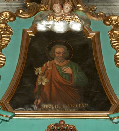 Zdjęcie nr 1: Obraz w formie trapezu o wklęsłych bokach i ściętych dolnych narożach, zamkniętego przerwanym obłokami łukiem odcinkowym nadwieszonym. Święty ukazany w półpostaci, frontalnie, lewą dłoń kładzie na piersi, w prawej opuszczonej wzdłuż ciała trzyma gałązkę lilii. Twarz ma pociągłą, o wąskich oczach, prostym nosie i małych ustach, okoloną krótką siwą brodą i włosami. Wokół głowy nimb. Ubrany jest w luźną zieloną tunikę ze złoconą lamówką oraz przewiązany diagonalnie przez prawe ramię pomarańczowy płaszcz. Postać ukazana na jednolitym czarnym tle. U dołu obrazu złocony napis „«JDŹCIE do JÓZEFA» / (Ks. I Moj. R. 41 W. 55”.
