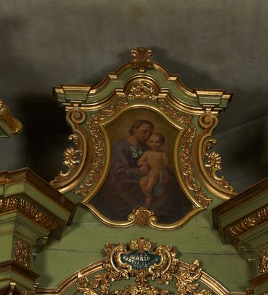 Zdjęcie nr 13: Nastawa ołtarzowa architektoniczna, jednoosiowa, jednokondygnacyjna ze zwieńczeniem, na cokole z czterema prostopadłościennymi postumentami wydzielonymi po bokach, z bramkami. Ołtarz drewniany, prostopadłościenny, z kamienną mensą z portatylem. Antependium drewniane obite miedzianą blachą, w formie leżącego prostokąta, ujętego profilowaną ramą, podzielone na dziesięć pól pasami z ornamentem geometrycznym, oraz aplikami w formie rautów na ich skrzyżowaniu. W środkowym polu monogram Marii oraz dwie apliki z orłem i pogonią u spodu. 
Retabulum flankowane ustawionymi schodkowo i zwróconymi na zewnątrz dwiema parami korynckich kolumn, umieszczonych na tle pilastrów oraz zewnętrzną parą pilastrów dekorowanych kwiatowymi zwisami. Podpory stoją na cokołach, podtrzymują wyłamane belkowanie, przerwane nad polem środkowym, oraz fragmenty przerwanego, falistego przyczółka z siedzącymi na obłokach puttami. W polu środkowym wnęka w formie stojącego prostokąta zamkniętego łukiem półkolistym nadwieszonym z uskokiem w profilowanej ramie, z obrazem św. Marcina. Pole środkowe zamknięte gzymsem przyjmującym kształt łuku odcinkowego nadwieszonego z rokokowym kartuszem z napisem "AVE / MARIA / GRATIA PLENA / LUC. 1.28" oraz z podwieszonymi dwiema różanymi gałązkami. Obraz flankowany dwoma zwisami na wstędze utworzonymi z kwiatów. Kondygnacja ujęta ażurowymi uszami utworzonymi z rocaille'u, kratki i kwiatów. Zwieńczenie w formie zbliżonej po stojącego prostokąta o wklęsłych bokach ujętych spływami wolutowymi z rocaille'm, zamkniętego gzymsem przyjmującym kształt łuku półkolistego nadwieszonego z uskokiem, wyłamanego przy krawędziach, zwieńczonego anthemionem. W polu obraz św. Józefa z Dzieciątkiem w formie zbliżonej do trapezu o wklęsłych bokach i wypukłych podstawach, w ramie. Ujęty z trzech stron wicią roślinną. Bramki na wysokości cokołu nastawy, w formie półkolistych, profilowanych arkad podtrzymywanych na pilastrach o kanelowanych trzonach. Arkady zwieńczone cokołami, na których ustawione są figury św. Wojciecha i św. Stanisława. Struktura polichromowana w kolorze seledynowym, ze złoconymi kolumnami, profilami i ornamentyką.


