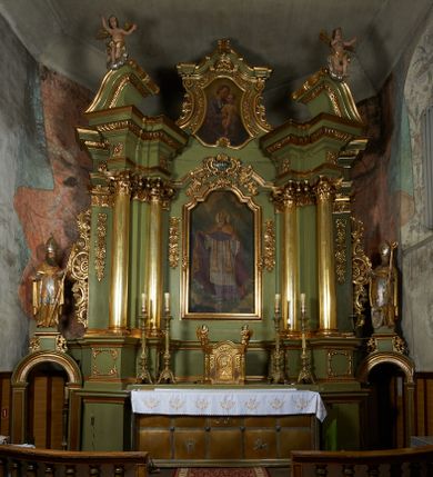 Zdjęcie nr 1: Nastawa ołtarzowa architektoniczna, jednoosiowa, jednokondygnacyjna ze zwieńczeniem, na cokole z czterema prostopadłościennymi postumentami wydzielonymi po bokach, z bramkami. Ołtarz drewniany, prostopadłościenny, z kamienną mensą z portatylem. Antependium drewniane obite miedzianą blachą, w formie leżącego prostokąta, ujętego profilowaną ramą, podzielone na dziesięć pól pasami z ornamentem geometrycznym, oraz aplikami w formie rautów na ich skrzyżowaniu. W środkowym polu monogram Marii oraz dwie apliki z orłem i pogonią u spodu. 
Retabulum flankowane ustawionymi schodkowo i zwróconymi na zewnątrz dwiema parami korynckich kolumn, umieszczonych na tle pilastrów oraz zewnętrzną parą pilastrów dekorowanych kwiatowymi zwisami. Podpory stoją na cokołach, podtrzymują wyłamane belkowanie, przerwane nad polem środkowym, oraz fragmenty przerwanego, falistego przyczółka z siedzącymi na obłokach puttami. W polu środkowym wnęka w formie stojącego prostokąta zamkniętego łukiem półkolistym nadwieszonym z uskokiem w profilowanej ramie, z obrazem św. Marcina. Pole środkowe zamknięte gzymsem przyjmującym kształt łuku odcinkowego nadwieszonego z rokokowym kartuszem z napisem "AVE / MARIA / GRATIA PLENA / LUC. 1.28" oraz z podwieszonymi dwiema różanymi gałązkami. Obraz flankowany dwoma zwisami na wstędze utworzonymi z kwiatów. Kondygnacja ujęta ażurowymi uszami utworzonymi z rocaille'u, kratki i kwiatów. Zwieńczenie w formie zbliżonej po stojącego prostokąta o wklęsłych bokach ujętych spływami wolutowymi z rocaille'm, zamkniętego gzymsem przyjmującym kształt łuku półkolistego nadwieszonego z uskokiem, wyłamanego przy krawędziach, zwieńczonego anthemionem. W polu obraz św. Józefa z Dzieciątkiem w formie zbliżonej do trapezu o wklęsłych bokach i wypukłych podstawach, w ramie. Ujęty z trzech stron wicią roślinną. Bramki na wysokości cokołu nastawy, w formie półkolistych, profilowanych arkad podtrzymywanych na pilastrach o kanelowanych trzonach. Arkady zwieńczone cokołami, na których ustawione są figury św. Wojciecha i św. Stanisława. Struktura polichromowana w kolorze seledynowym, ze złoconymi kolumnami, profilami i ornamentyką.


