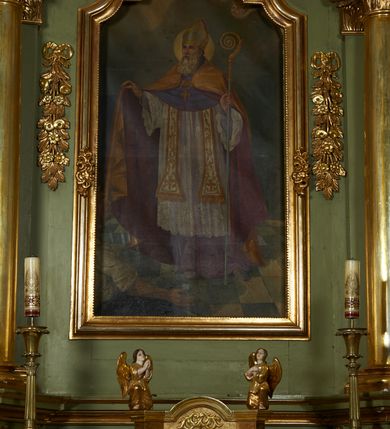 Zdjęcie nr 39: Nastawa ołtarzowa architektoniczna, jednoosiowa, jednokondygnacyjna ze zwieńczeniem, na cokole z czterema prostopadłościennymi postumentami wydzielonymi po bokach, z bramkami. Ołtarz drewniany, prostopadłościenny, z kamienną mensą z portatylem. Antependium drewniane obite miedzianą blachą, w formie leżącego prostokąta, ujętego profilowaną ramą, podzielone na dziesięć pól pasami z ornamentem geometrycznym, oraz aplikami w formie rautów na ich skrzyżowaniu. W środkowym polu monogram Marii oraz dwie apliki z orłem i pogonią u spodu. 
Retabulum flankowane ustawionymi schodkowo i zwróconymi na zewnątrz dwiema parami korynckich kolumn, umieszczonych na tle pilastrów oraz zewnętrzną parą pilastrów dekorowanych kwiatowymi zwisami. Podpory stoją na cokołach, podtrzymują wyłamane belkowanie, przerwane nad polem środkowym, oraz fragmenty przerwanego, falistego przyczółka z siedzącymi na obłokach puttami. W polu środkowym wnęka w formie stojącego prostokąta zamkniętego łukiem półkolistym nadwieszonym z uskokiem w profilowanej ramie, z obrazem św. Marcina. Pole środkowe zamknięte gzymsem przyjmującym kształt łuku odcinkowego nadwieszonego z rokokowym kartuszem z napisem "AVE / MARIA / GRATIA PLENA / LUC. 1.28" oraz z podwieszonymi dwiema różanymi gałązkami. Obraz flankowany dwoma zwisami na wstędze utworzonymi z kwiatów. Kondygnacja ujęta ażurowymi uszami utworzonymi z rocaille'u, kratki i kwiatów. Zwieńczenie w formie zbliżonej po stojącego prostokąta o wklęsłych bokach ujętych spływami wolutowymi z rocaille'm, zamkniętego gzymsem przyjmującym kształt łuku półkolistego nadwieszonego z uskokiem, wyłamanego przy krawędziach, zwieńczonego anthemionem. W polu obraz św. Józefa z Dzieciątkiem w formie zbliżonej do trapezu o wklęsłych bokach i wypukłych podstawach, w ramie. Ujęty z trzech stron wicią roślinną. Bramki na wysokości cokołu nastawy, w formie półkolistych, profilowanych arkad podtrzymywanych na pilastrach o kanelowanych trzonach. Arkady zwieńczone cokołami, na których ustawione są figury św. Wojciecha i św. Stanisława. Struktura polichromowana w kolorze seledynowym, ze złoconymi kolumnami, profilami i ornamentyką.


