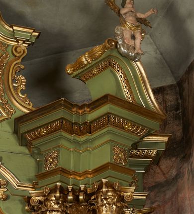 Zdjęcie nr 46: Nastawa ołtarzowa architektoniczna, jednoosiowa, jednokondygnacyjna ze zwieńczeniem, na cokole z czterema prostopadłościennymi postumentami wydzielonymi po bokach, z bramkami. Ołtarz drewniany, prostopadłościenny, z kamienną mensą z portatylem. Antependium drewniane obite miedzianą blachą, w formie leżącego prostokąta, ujętego profilowaną ramą, podzielone na dziesięć pól pasami z ornamentem geometrycznym, oraz aplikami w formie rautów na ich skrzyżowaniu. W środkowym polu monogram Marii oraz dwie apliki z orłem i pogonią u spodu. 
Retabulum flankowane ustawionymi schodkowo i zwróconymi na zewnątrz dwiema parami korynckich kolumn, umieszczonych na tle pilastrów oraz zewnętrzną parą pilastrów dekorowanych kwiatowymi zwisami. Podpory stoją na cokołach, podtrzymują wyłamane belkowanie, przerwane nad polem środkowym, oraz fragmenty przerwanego, falistego przyczółka z siedzącymi na obłokach puttami. W polu środkowym wnęka w formie stojącego prostokąta zamkniętego łukiem półkolistym nadwieszonym z uskokiem w profilowanej ramie, z obrazem św. Marcina. Pole środkowe zamknięte gzymsem przyjmującym kształt łuku odcinkowego nadwieszonego z rokokowym kartuszem z napisem &quot;AVE / MARIA / GRATIA PLENA / LUC. 1.28&quot; oraz z podwieszonymi dwiema różanymi gałązkami. Obraz flankowany dwoma zwisami na wstędze utworzonymi z kwiatów. Kondygnacja ujęta ażurowymi uszami utworzonymi z rocaille&#039;u, kratki i kwiatów. Zwieńczenie w formie zbliżonej po stojącego prostokąta o wklęsłych bokach ujętych spływami wolutowymi z rocaille&#039;m, zamkniętego gzymsem przyjmującym kształt łuku półkolistego nadwieszonego z uskokiem, wyłamanego przy krawędziach, zwieńczonego anthemionem. W polu obraz św. Józefa z Dzieciątkiem w formie zbliżonej do trapezu o wklęsłych bokach i wypukłych podstawach, w ramie. Ujęty z trzech stron wicią roślinną. Bramki na wysokości cokołu nastawy, w formie półkolistych, profilowanych arkad podtrzymywanych na pilastrach o kanelowanych trzonach. Arkady zwieńczone cokołami, na których ustawione są figury św. Wojciecha i św. Stanisława. Struktura polichromowana w kolorze seledynowym, ze złoconymi kolumnami, profilami i ornamentyką.


