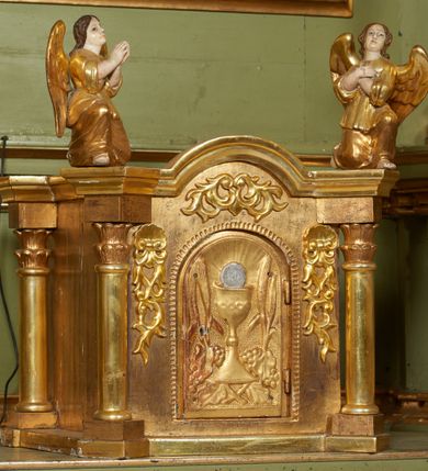 Zdjęcie nr 27: Nastawa ołtarzowa architektoniczna, jednoosiowa, jednokondygnacyjna ze zwieńczeniem, na cokole z czterema prostopadłościennymi postumentami wydzielonymi po bokach, z bramkami. Ołtarz drewniany, prostopadłościenny, z kamienną mensą z portatylem. Antependium drewniane obite miedzianą blachą, w formie leżącego prostokąta, ujętego profilowaną ramą, podzielone na dziesięć pól pasami z ornamentem geometrycznym, oraz aplikami w formie rautów na ich skrzyżowaniu. W środkowym polu monogram Marii oraz dwie apliki z orłem i pogonią u spodu. 
Retabulum flankowane ustawionymi schodkowo i zwróconymi na zewnątrz dwiema parami korynckich kolumn, umieszczonych na tle pilastrów oraz zewnętrzną parą pilastrów dekorowanych kwiatowymi zwisami. Podpory stoją na cokołach, podtrzymują wyłamane belkowanie, przerwane nad polem środkowym, oraz fragmenty przerwanego, falistego przyczółka z siedzącymi na obłokach puttami. W polu środkowym wnęka w formie stojącego prostokąta zamkniętego łukiem półkolistym nadwieszonym z uskokiem w profilowanej ramie, z obrazem św. Marcina. Pole środkowe zamknięte gzymsem przyjmującym kształt łuku odcinkowego nadwieszonego z rokokowym kartuszem z napisem &quot;AVE / MARIA / GRATIA PLENA / LUC. 1.28&quot; oraz z podwieszonymi dwiema różanymi gałązkami. Obraz flankowany dwoma zwisami na wstędze utworzonymi z kwiatów. Kondygnacja ujęta ażurowymi uszami utworzonymi z rocaille&#039;u, kratki i kwiatów. Zwieńczenie w formie zbliżonej po stojącego prostokąta o wklęsłych bokach ujętych spływami wolutowymi z rocaille&#039;m, zamkniętego gzymsem przyjmującym kształt łuku półkolistego nadwieszonego z uskokiem, wyłamanego przy krawędziach, zwieńczonego anthemionem. W polu obraz św. Józefa z Dzieciątkiem w formie zbliżonej do trapezu o wklęsłych bokach i wypukłych podstawach, w ramie. Ujęty z trzech stron wicią roślinną. Bramki na wysokości cokołu nastawy, w formie półkolistych, profilowanych arkad podtrzymywanych na pilastrach o kanelowanych trzonach. Arkady zwieńczone cokołami, na których ustawione są figury św. Wojciecha i św. Stanisława. Struktura polichromowana w kolorze seledynowym, ze złoconymi kolumnami, profilami i ornamentyką.


