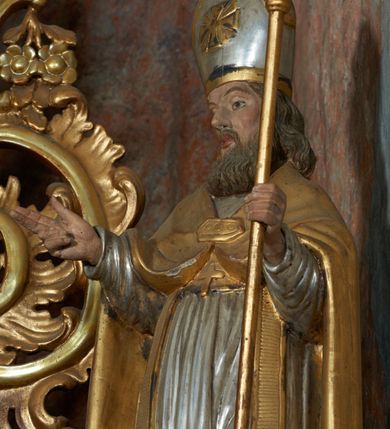 Zdjęcie nr 19: Nastawa ołtarzowa architektoniczna, jednoosiowa, jednokondygnacyjna ze zwieńczeniem, na cokole z czterema prostopadłościennymi postumentami wydzielonymi po bokach, z bramkami. Ołtarz drewniany, prostopadłościenny, z kamienną mensą z portatylem. Antependium drewniane obite miedzianą blachą, w formie leżącego prostokąta, ujętego profilowaną ramą, podzielone na dziesięć pól pasami z ornamentem geometrycznym, oraz aplikami w formie rautów na ich skrzyżowaniu. W środkowym polu monogram Marii oraz dwie apliki z orłem i pogonią u spodu. 
Retabulum flankowane ustawionymi schodkowo i zwróconymi na zewnątrz dwiema parami korynckich kolumn, umieszczonych na tle pilastrów oraz zewnętrzną parą pilastrów dekorowanych kwiatowymi zwisami. Podpory stoją na cokołach, podtrzymują wyłamane belkowanie, przerwane nad polem środkowym, oraz fragmenty przerwanego, falistego przyczółka z siedzącymi na obłokach puttami. W polu środkowym wnęka w formie stojącego prostokąta zamkniętego łukiem półkolistym nadwieszonym z uskokiem w profilowanej ramie, z obrazem św. Marcina. Pole środkowe zamknięte gzymsem przyjmującym kształt łuku odcinkowego nadwieszonego z rokokowym kartuszem z napisem "AVE / MARIA / GRATIA PLENA / LUC. 1.28" oraz z podwieszonymi dwiema różanymi gałązkami. Obraz flankowany dwoma zwisami na wstędze utworzonymi z kwiatów. Kondygnacja ujęta ażurowymi uszami utworzonymi z rocaille'u, kratki i kwiatów. Zwieńczenie w formie zbliżonej po stojącego prostokąta o wklęsłych bokach ujętych spływami wolutowymi z rocaille'm, zamkniętego gzymsem przyjmującym kształt łuku półkolistego nadwieszonego z uskokiem, wyłamanego przy krawędziach, zwieńczonego anthemionem. W polu obraz św. Józefa z Dzieciątkiem w formie zbliżonej do trapezu o wklęsłych bokach i wypukłych podstawach, w ramie. Ujęty z trzech stron wicią roślinną. Bramki na wysokości cokołu nastawy, w formie półkolistych, profilowanych arkad podtrzymywanych na pilastrach o kanelowanych trzonach. Arkady zwieńczone cokołami, na których ustawione są figury św. Wojciecha i św. Stanisława. Struktura polichromowana w kolorze seledynowym, ze złoconymi kolumnami, profilami i ornamentyką.


