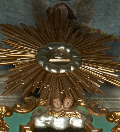 Zdjęcie nr 18: Nastawa ołtarzowa architektoniczna, jednoosiowa, jednokondygnacyjna ze zwieńczeniem, ustawiona na cokole z dwoma prostopadłościennymi postumentami wydzielonymi po bokach, z bramkami w partii cokołu. Ołtarz drewniany, prostopadłościenny, zwężający się ku dołowi, dekorowany z przodu rzeźbionym wieńcem z monogramem Marii, mensa drewniana. Na mensie ustawione tabernakulum w formie drewnianej skrzynki o ściętych przednich narożach, flankowanej parą kolumienek. Drzwiczki w formie stojącego prostokąta dekorowane płyciną. Nastawa ołtarzowa ujęta parą kolumn o stylizowanych kapitelach kompozytowych dźwigających pełne belkowanie, przerwane nad polem środkowym, oraz fragmenty przerwanego, półkolistego przyczółka, na którym klęczą na obłokach dwa putta. Fryz dekorowany ornamentem roślinnym zbliżonym do akantu. W polu głównym wnęka w formie stojącego prostokąta w profilowanej ramie, z obrazem Koronacji Marii. Nad nim medalion utworzony z akantu z monogramem Marii, zwieńczony koroną zamkniętą. Zwieńczenie w formie trapezu, którego brzegi dekorowane są stylizowanym rocaille&#039;m tworzącym uszaki. W polu obraz św. Józefa w formie trapezu o ściętych dolnych narożach, zamkniętego łukiem półkolistym nadwieszonym, w profilowanej ramie, z łukiem częściowo przesłoniętym obłokami z dwoma uskrzydlonymi główkami anielskimi. Nastawa zakończona medalionem z obłoków z Okiem Opatrzności w glorii promienistej. Nastawę flankują bramki w partii cokołu z przejściami w formie stojącego prostokąta zamkniętego łukiem odcinkowym nadwieszonym, zakończone profilowanym gzymsem oraz cokołami dekorowanymi roślinnymi konsolami, na których stoją figury św. Anny i św. Joachima. Struktura polichromowana w kolorze seledynowym, ze złoconymi kolumnami, profilami i  ornamentyką. 
