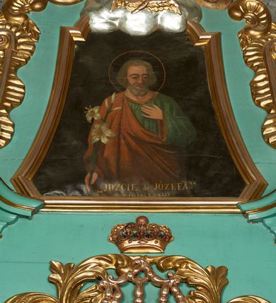 Zdjęcie nr 17: Nastawa ołtarzowa architektoniczna, jednoosiowa, jednokondygnacyjna ze zwieńczeniem, ustawiona na cokole z dwoma prostopadłościennymi postumentami wydzielonymi po bokach, z bramkami w partii cokołu. Ołtarz drewniany, prostopadłościenny, zwężający się ku dołowi, dekorowany z przodu rzeźbionym wieńcem z monogramem Marii, mensa drewniana. Na mensie ustawione tabernakulum w formie drewnianej skrzynki o ściętych przednich narożach, flankowanej parą kolumienek. Drzwiczki w formie stojącego prostokąta dekorowane płyciną. Nastawa ołtarzowa ujęta parą kolumn o stylizowanych kapitelach kompozytowych dźwigających pełne belkowanie, przerwane nad polem środkowym, oraz fragmenty przerwanego, półkolistego przyczółka, na którym klęczą na obłokach dwa putta. Fryz dekorowany ornamentem roślinnym zbliżonym do akantu. W polu głównym wnęka w formie stojącego prostokąta w profilowanej ramie, z obrazem Koronacji Marii. Nad nim medalion utworzony z akantu z monogramem Marii, zwieńczony koroną zamkniętą. Zwieńczenie w formie trapezu, którego brzegi dekorowane są stylizowanym rocaille'm tworzącym uszaki. W polu obraz św. Józefa w formie trapezu o ściętych dolnych narożach, zamkniętego łukiem półkolistym nadwieszonym, w profilowanej ramie, z łukiem częściowo przesłoniętym obłokami z dwoma uskrzydlonymi główkami anielskimi. Nastawa zakończona medalionem z obłoków z Okiem Opatrzności w glorii promienistej. Nastawę flankują bramki w partii cokołu z przejściami w formie stojącego prostokąta zamkniętego łukiem odcinkowym nadwieszonym, zakończone profilowanym gzymsem oraz cokołami dekorowanymi roślinnymi konsolami, na których stoją figury św. Anny i św. Joachima. Struktura polichromowana w kolorze seledynowym, ze złoconymi kolumnami, profilami i  ornamentyką. 
