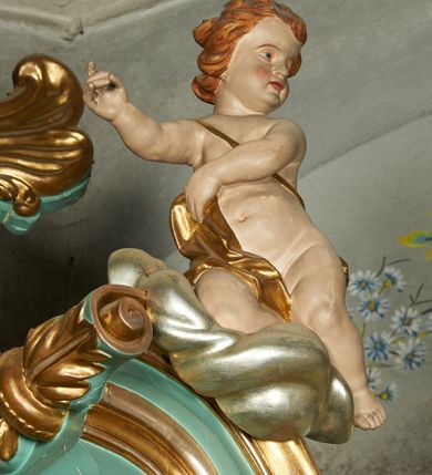 Zdjęcie nr 12: Nastawa ołtarzowa architektoniczna, jednoosiowa, jednokondygnacyjna ze zwieńczeniem, ustawiona na cokole z dwoma prostopadłościennymi postumentami wydzielonymi po bokach, z bramkami w partii cokołu. Ołtarz drewniany, prostopadłościenny, zwężający się ku dołowi, dekorowany z przodu rzeźbionym wieńcem z monogramem Marii, mensa drewniana. Na mensie ustawione tabernakulum w formie drewnianej skrzynki o ściętych przednich narożach, flankowanej parą kolumienek. Drzwiczki w formie stojącego prostokąta dekorowane płyciną. Nastawa ołtarzowa ujęta parą kolumn o stylizowanych kapitelach kompozytowych dźwigających pełne belkowanie, przerwane nad polem środkowym, oraz fragmenty przerwanego, półkolistego przyczółka, na którym klęczą na obłokach dwa putta. Fryz dekorowany ornamentem roślinnym zbliżonym do akantu. W polu głównym wnęka w formie stojącego prostokąta w profilowanej ramie, z obrazem Koronacji Marii. Nad nim medalion utworzony z akantu z monogramem Marii, zwieńczony koroną zamkniętą. Zwieńczenie w formie trapezu, którego brzegi dekorowane są stylizowanym rocaille&#039;m tworzącym uszaki. W polu obraz św. Józefa w formie trapezu o ściętych dolnych narożach, zamkniętego łukiem półkolistym nadwieszonym, w profilowanej ramie, z łukiem częściowo przesłoniętym obłokami z dwoma uskrzydlonymi główkami anielskimi. Nastawa zakończona medalionem z obłoków z Okiem Opatrzności w glorii promienistej. Nastawę flankują bramki w partii cokołu z przejściami w formie stojącego prostokąta zamkniętego łukiem odcinkowym nadwieszonym, zakończone profilowanym gzymsem oraz cokołami dekorowanymi roślinnymi konsolami, na których stoją figury św. Anny i św. Joachima. Struktura polichromowana w kolorze seledynowym, ze złoconymi kolumnami, profilami i  ornamentyką. 
