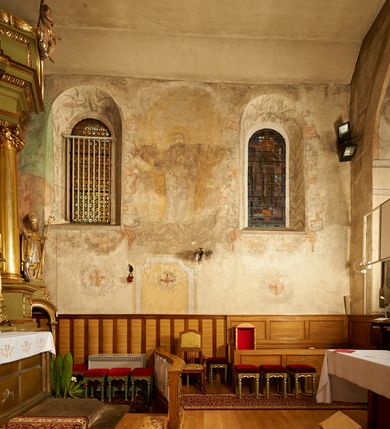 Zdjęcie nr 10: Na ścianie wschodniej prezbiterium namalowany zielono-niebieski paludament z czerwoną podszewką, flankujący ołtarz główny. Na ścianie południowej dwa okna ujęte są malowanymi obramieniami utworzonymi z ornamentu kartuszowo-zawijanego (rollwerk), wzdłuż dolnej krawędzi mają podwieszone girlandy owocowo-roślinne. W szerokich rozglifieniach okien malowany ornament kandelabrowy. W polu pomiędzy oknami fragmenty sceny figuralnej przedstawiającej Chrystusa w typie Salvator Mundi na tle gęstych, szaro-żółtych obłoków. Postać ukazana frontalnie, lewą ręką podtrzymuje kulę, praw unosi w geście błogosławieństwa. Twarz ma kwadratową, o wąskich, migdałowatych oczach, dużym, prostym nosie i wąskich ustach, okoloną krótką brodą oraz włosami sięgającymi ramion. Wokół głowy nimb. Postać ubrana w długą, biało-różową tunikę. Na ścianie północnej kamienny portal do zakrystii ujęty jest obramieniem utworzonym z ornamentu kartuszowo-zawijanego. 
W podniebiu łuku tęczowego polichromia z przedstawieniem gołębicy Ducha Świętego w glorii promienistej w szczycie podłucza, flankowanej przez słońce i księżyc pośród szarych, gęstych obłoków. Poniżej dwa anioły z arma Christi, pośród szarych chmur, zwrócone w trzech czwartych w stronę prezbiterium. Postacie o owalnych twarzach, z okrągłymi oczami skierowanymi w dół, dużymi nosami i wąskimi ustami, okolone włosami sięgającymi ramion. Ubrane są w jasnobrązowe tuniki. Anioł na południowej stronie trzyma drabinę, sznur, bicz i koronę cierniową. Anioł na północnej stronie łuku – włócznię, włócznię z nabitą gąbką oraz liść palmy. Na północnej stronie łuku, poniżej ambony fragment malowanej czerwonej tkaniny. Krawędź łuku tęczowego od strony nawy obwiedziona obramieniem utworzonym w ornamentu kartuszowo-zawijanego. 
Pięć zacheuszków na ścianach północnej i południowej w formie okrągłych medalionów z krzyżami równoramiennymi w polach, ujęte dekoracyjnym pasem, w wieńcach laurowych.