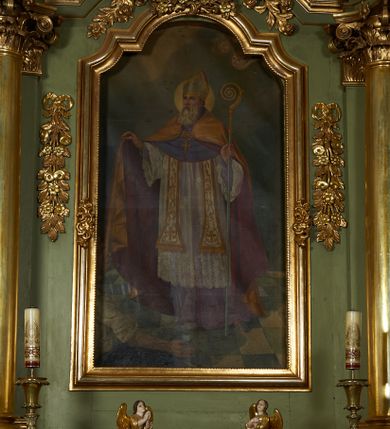 Zdjęcie nr 2: Tabernakulum w formie drewnianej skrzynki ustawionej na niskiej podstawie, ujęte w czterech narożach ukośnie zwróconymi cokołami z kolumnami dźwigającymi imposty oraz profilowany gzyms opasujący całość, nad ścianką frontową przyjmujący kształt łuku odcinkowego. Drzwiczki w formie stojącego prostokąta zamkniętego łukiem półkolistym, dekorowane płaskorzeźbionym przedstawieniem kielicha z hostią, flankowanego winnym gronem i kłosami zbóż. Drzwiczki ujęte z trzech stron ornamentem roślinnym. Na gzymsie dwie figurki klęczących  aniołów. Tabernakulum w całości pozłocone. 

