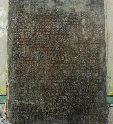 Zdjęcie nr 1: Płyta w formie stojącego prostokąta. W polu złocona inskrypcja: „D[EO] O[PTIMO] M[AXIMO] / ZIMNY MARMVR POKRIWAM PROCHV MIZERNEGO / SCZVPLA RESZTE KTORA TV DNIA CZEKA SADNEGO. / TE SZYMON Z KALINOWA KALINOWSKI W GROBIE / ZŁOZYŁ VPODOBAWSZY ODPOCYNEK SOBIE / PO WOIENNYCH FATIGACH KTORE Z KONIECPOLSKIEM / ZOSTAIAC KASTELANEM NA ONCZASZ KRAKOWSKIM / WODZEM SWOIM PONOSIEŁ MALBORSKIE SWIADKAMI / MVRY IAK MEZNIE STAWIAŁ W BITWIE ZE SZWEDA[M]I / SWIADKIEM CZVDNOW KOZACKA GDZIE SPRZISIEGŁA SIE A / ZDVMNEM MOSKALEM ZGVBE OYCZYZNIE WROZYŁA / IAK KAWALERSKO STAWAŁ GDZIE PRZESZ WOYSKA MESTWO / WSPANIAŁE ODEBRAŁA KORONA ZWYCIESTWO / POTYM GDY NOWE BVNTY KOZACZTWO WZNIECIEŁO / ZA DNIEPREM A WOYSKO SIE KORONNE SKUPIEŁO / POD GŁVCHOW BYŁ W POTRZEBIE DZIELNOSC V WAZONO / I W PODNIESTRZV ZAWODZIC STRAZE  MV ZLECONO. / W PRETCZE  ZAS GDY CZESC WOISKA POD TARNOPOL STAWA / WODZ IEMV STRAZNIKOSTWO WOYSKOWE ODDAWA / Z POCHWAŁA TO ODPRAWIEŁ BIEŁ SIE POTYM MEZNIE / NA BATOHV Z TATARY TESZ ORDE POTESZNIE / POD KALVSZA KVMARNEM GROMIEŁ YZ TVRKAMI / VGANIAŁ SIE WIELEKROC WSZYKV Y HARCAMI / SKONCZYŁ WOYNE KRWIA TVRSKA POLA NAPOIWSZY / CHOCIMSKIE A ZIEMIANSKI ZYWOT VLVBIWSZY / W TYM KOSCIELE GOEZINKI NIEPOKALANEGO / FVNDOWAŁ MATKO BOSKA POCZECIA TWOIEGO. / WIEC ZA TRVDY WOIENNE CZEKAIAC KORONY / DO TWEI SIE PANI SWIATA VCIEKA OBRONY / VPROS MV ZYWOT WIECZNY WSZAK MV NIENOWINA / BYLO LAC KREW ZA CALOSC WIARY TWEGO SYNA / VMARŁ DNIA [...] ROKV [...] / WIEKV SWEGO LAT [...]”. W górnym lewym rogu płyty ryty herb Ślepowron z inskrypcją: „[Z DOMV KALINOWSKI]CH ZRODZICA”. W górnym prawym rogu ryty herb Gozdawa z inskrypcją: „[Z DOMV SOKO]/LOWSKICH ZM[ATKI]”. W dolnym lewym rogu herb Pilawa z inskrypcją: „[Z] DOMV POROWSK/[I]CH PRABABY”. W dolnym prawym rogu herb Massalski z inskrypcją: „Z DOMV MASS/ALSKICH ZBABY”. 


