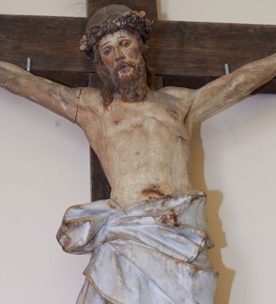 Zdjęcie nr 1: Figura Chrystusa żywego przybitego trzema gwoździami do prostego krzyża. Ciało w lekkim zwisie, o szeroko rozłożonych ramionach, lekko łukowato wygiętych, głowa przechylona na prawy bark, nogi wyprostowane, stopy skrzyżowane w układzie prawa na lewą. Twarz ma podłużną, o półprzymkniętych oczach, małym nosie i pełnych ustach, okoloną falowaną brodą i włosami sięgającymi ramion. Na głowie korona cierniowa. Ciało szczupłe, muskularne, o delikatnie podkreślonym modelunku klatki piersiowej i ramion. Biodra przesłonięte obszernym, silnie drapowanym, białym perizonium ze złoconą lamówką, sięgającym połowy uda, zawiązanym na prawym boku, z długim zwisem tkaniny wzdłuż prawej nogi. Polichromia ciała naturalistyczna z zaznaczonymi śladami męki. 