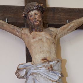 Zdjęcie nr 1: Figura Chrystusa żywego przybitego trzema gwoździami do prostego krzyża. Ciało w lekkim zwisie, o szeroko rozłożonych ramionach, lekko łukowato wygiętych, głowa przechylona na prawy bark, nogi wyprostowane, stopy skrzyżowane w układzie prawa na lewą. Twarz ma podłużną, o półprzymkniętych oczach, małym nosie i pełnych ustach, okoloną falowaną brodą i włosami sięgającymi ramion. Na głowie korona cierniowa. Ciało szczupłe, muskularne, o delikatnie podkreślonym modelunku klatki piersiowej i ramion. Biodra przesłonięte obszernym, silnie drapowanym, białym perizonium ze złoconą lamówką, sięgającym połowy uda, zawiązanym na prawym boku, z długim zwisem tkaniny wzdłuż prawej nogi. Polichromia ciała naturalistyczna z zaznaczonymi śladami męki. 
