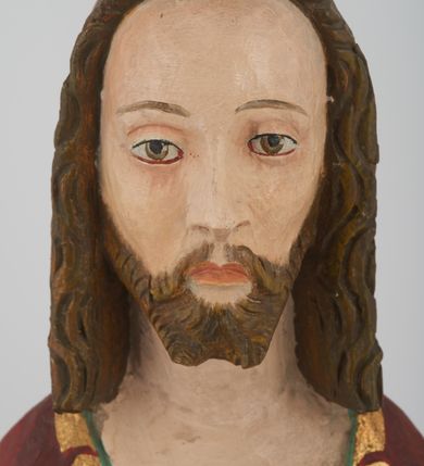 Zdjęcie nr 6: Figura Chrystusa pełnoplastyczna, ustawiona na podstawie na planie ośmioboku oraz na rzeźbionym fragmencie podłoża. Chrystus zwrócony jest frontalnie, w lekkim kontrapoście. Prawą rękę unosi w geście błogosławieństwa, w lewej trzyma drzewce czerwonej chorągwi z tkaniny z naszytym krzyżem, ujętej dwoma chwostami. Twarz ma pociągłą z wysokim czołem, migdałowatymi oczami, wąskim i zadartym nosem oraz małymi ustami, okoloną krótką, falowaną brodą rozdzieloną na dwoje oraz regularnie falowanymi włosami sięgającymi ramion. Ubrany jest w czerwony płaszcz z zieloną podszewką i złoconą lamówką, zapięty na piersi, opadający na plecy i ramiona, zawinięty łukowato z przodu postaci, odsłaniający nagi tors i lewą nogę. Polichromia ciała naturalistyczna z zaznaczonymi śladami męki.