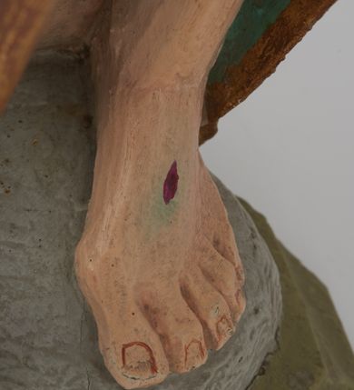 Zdjęcie nr 7: Figura Chrystusa pełnoplastyczna, ustawiona na podstawie na planie ośmioboku oraz na rzeźbionym fragmencie podłoża. Chrystus zwrócony jest frontalnie, w lekkim kontrapoście. Prawą rękę unosi w geście błogosławieństwa, w lewej trzyma drzewce czerwonej chorągwi z tkaniny z naszytym krzyżem, ujętej dwoma chwostami. Twarz ma pociągłą z wysokim czołem, migdałowatymi oczami, wąskim i zadartym nosem oraz małymi ustami, okoloną krótką, falowaną brodą rozdzieloną na dwoje oraz regularnie falowanymi włosami sięgającymi ramion. Ubrany jest w czerwony płaszcz z zieloną podszewką i złoconą lamówką, zapięty na piersi, opadający na plecy i ramiona, zawinięty łukowato z przodu postaci, odsłaniający nagi tors i lewą nogę. Polichromia ciała naturalistyczna z zaznaczonymi śladami męki.