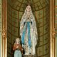 Zdjęcie nr 1: Grupa rzeźbiarska złożona z pełnoplastycznej figury Marii stojącej na cokole i na rzeźbionym fragmencie skały oraz z klęczącej na osobnym cokole i podstawie po prawej stronie Marii pełnoplastycznej figury Bernadety Soubirous. Maria ukazana frontalnie, w całej postaci, w wykroku, z uniesioną głową oraz rękami złożonymi w geście modlitwy. Twarz ma pociągłą, o łagodnych rysach, oczach skierowanych w górę, prostym nosie oraz małych ustach. Ubrana jest w białą, długą suknię, dekorowaną złoconymi rozetami oraz lamówką, przepasaną w talii niebieską szarfą ze złoconymi gwiazdkami i brzegami, zawiązaną z przodu. Na głowę i ramiona ma narzucony biały płaszcz zdobiony złoconymi rozetami i wicią roślinną przy brzegach, ze srebrzonymi pasami na podszewce, spływający kaskadowo po bokach postaci. Na głowie ma złoconą koronę otwartą, wokół niej nimb gwieździsty. Na przedramionach ma zawieszony różaniec. Na stopach złocone róże. Bernadeta zwrócona jest w trzech czwartych w lewo, z uniesioną głową, w lewej dłoni trzyma krzyż z różańca Marii, prawą kładzie na piersi. Twarz ma owalną, o młodzieńczych rysach, migdałowatych oczach, prostym nosie i małych ustach. Ubrana jest w brązową suknię z zieloną zapaską przewiązaną w talii oraz zarzuconą na plecy i skrzyżowaną na piersi jasnobrązową chustę w kratę, na głowie ma biały welon. 