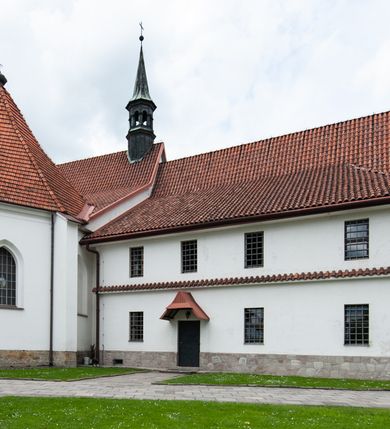 Zdjęcie nr 18: Kościół murowany z cegły i kamienia, tynkowany, orientowany, jednonawowy z kaplicami. Prezbiterium wydłużone, zamknięte trójbocznie, odchylone na południe od osi nawy, przy północnej ścianie niewielka, prostokątna dawna zakrystia (obecnie kruchta), przy południowej dobudowana wtórnie piętrowa dwuczęściowa zakrystia ze skarbcem, od wschodu, na zewnętrznej ścianie kościoła Ogrojec. Nawa główna szersza od prezbiterium, na rzucie prostokąta, od południa wieloboczna kaplica Najświętszego Serca Pana Jezusa (dawniej Przemienienia Pańskiego), od północy i południa dobudowane kaplice boczne na planie prostokąta, północna dwukrotnie większa od południowej, od zachodu wieża na planie kwadratu. Prezbiterium i nawa nakryte sklepieniami pozornymi, oddzielone od ścian gzymsem przebiegającym przez całe wnętrze, łuk tęczowy półkolisty, wewnątrz ujęty pilastrami. Dawne, ostrołukowe okna znajdują się w ścianach nawy głównej. Dostęp do kaplicy i naw bocznych z nawy głównej przez wysokie przejścia arkadowe, w północnej części nawy ujęte opaskami tynkowymi, w północno-zachodniej przejście z barokowym, kamiennym portalem (dawne wejście do kościoła). W starej zakrystii dwa gotyckie, kamienne, ostrołukowe portale oraz gotyckie okno. W wielobocznej kaplicy sklepienie kolebkowe z lunetami, w kaplicach bocznych oraz w nowej zakrystii stropy żelbetowe i sufity tynkowe. Elewacje tynkowane, z obłożoną kamieniem partią cokołu, ściana północna dawnej zakrystii z odsłoniętym wątkiem kamiennym oraz narożną przyporą, wieloboczna kaplica oszkarpowana w narożach. Do wschodniej ściany prezbiterium dobudowany kamienny Ogrójec z arkadą, zwieńczony gzymsem oraz schodkowym szczytem z kamiennymi figurami. Wejścia do kościoła przez kaplice boczne od północy i zachodu oraz przez kruchtę w przyziemiu wieży. Okna w formie stojącego prostokąta w ścianach kaplic bocznych, nowej zakrystii, prezbiterium, okna ostrołukowe w wielobocznej kaplicy. Wieża smukła, trójkondygnacyjna, bez podziałów architektonicznych z oknami na poziomie każdej kondygnacji, zwieńczona hełmem baniastym. Nawa główna i prezbiterium nakryte dachem dwuspadowym, niższe nawy boczne również. W miejscu połączenia nawy i prezbiterium wieżyczka na sygnaturkę. Kaplica przekryta dachem ostrosłupowym, nowa zakrystia i skarbiec dachem trójspadowym, stara zakrystia pulpitowym. 
