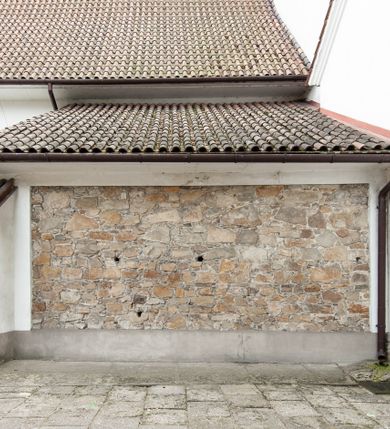 Zdjęcie nr 16: Kościół murowany z cegły i kamienia, tynkowany, orientowany, jednonawowy z kaplicami. Prezbiterium wydłużone, zamknięte trójbocznie, odchylone na południe od osi nawy, przy północnej ścianie niewielka, prostokątna dawna zakrystia (obecnie kruchta), przy południowej dobudowana wtórnie piętrowa dwuczęściowa zakrystia ze skarbcem, od wschodu, na zewnętrznej ścianie kościoła Ogrojec. Nawa główna szersza od prezbiterium, na rzucie prostokąta, od południa wieloboczna kaplica Najświętszego Serca Pana Jezusa (dawniej Przemienienia Pańskiego), od północy i południa dobudowane kaplice boczne na planie prostokąta, północna dwukrotnie większa od południowej, od zachodu wieża na planie kwadratu. Prezbiterium i nawa nakryte sklepieniami pozornymi, oddzielone od ścian gzymsem przebiegającym przez całe wnętrze, łuk tęczowy półkolisty, wewnątrz ujęty pilastrami. Dawne, ostrołukowe okna znajdują się w ścianach nawy głównej. Dostęp do kaplicy i naw bocznych z nawy głównej przez wysokie przejścia arkadowe, w północnej części nawy ujęte opaskami tynkowymi, w północno-zachodniej przejście z barokowym, kamiennym portalem (dawne wejście do kościoła). W starej zakrystii dwa gotyckie, kamienne, ostrołukowe portale oraz gotyckie okno. W wielobocznej kaplicy sklepienie kolebkowe z lunetami, w kaplicach bocznych oraz w nowej zakrystii stropy żelbetowe i sufity tynkowe. Elewacje tynkowane, z obłożoną kamieniem partią cokołu, ściana północna dawnej zakrystii z odsłoniętym wątkiem kamiennym oraz narożną przyporą, wieloboczna kaplica oszkarpowana w narożach. Do wschodniej ściany prezbiterium dobudowany kamienny Ogrójec z arkadą, zwieńczony gzymsem oraz schodkowym szczytem z kamiennymi figurami. Wejścia do kościoła przez kaplice boczne od północy i zachodu oraz przez kruchtę w przyziemiu wieży. Okna w formie stojącego prostokąta w ścianach kaplic bocznych, nowej zakrystii, prezbiterium, okna ostrołukowe w wielobocznej kaplicy. Wieża smukła, trójkondygnacyjna, bez podziałów architektonicznych z oknami na poziomie każdej kondygnacji, zwieńczona hełmem baniastym. Nawa główna i prezbiterium nakryte dachem dwuspadowym, niższe nawy boczne również. W miejscu połączenia nawy i prezbiterium wieżyczka na sygnaturkę. Kaplica przekryta dachem ostrosłupowym, nowa zakrystia i skarbiec dachem trójspadowym, stara zakrystia pulpitowym. 
