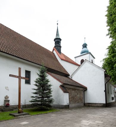 Zdjęcie nr 22: Kościół murowany z cegły i kamienia, tynkowany, orientowany, jednonawowy z kaplicami. Prezbiterium wydłużone, zamknięte trójbocznie, odchylone na południe od osi nawy, przy północnej ścianie niewielka, prostokątna dawna zakrystia (obecnie kruchta), przy południowej dobudowana wtórnie piętrowa dwuczęściowa zakrystia ze skarbcem, od wschodu, na zewnętrznej ścianie kościoła Ogrojec. Nawa główna szersza od prezbiterium, na rzucie prostokąta, od południa wieloboczna kaplica Najświętszego Serca Pana Jezusa (dawniej Przemienienia Pańskiego), od północy i południa dobudowane kaplice boczne na planie prostokąta, północna dwukrotnie większa od południowej, od zachodu wieża na planie kwadratu. Prezbiterium i nawa nakryte sklepieniami pozornymi, oddzielone od ścian gzymsem przebiegającym przez całe wnętrze, łuk tęczowy półkolisty, wewnątrz ujęty pilastrami. Dawne, ostrołukowe okna znajdują się w ścianach nawy głównej. Dostęp do kaplicy i naw bocznych z nawy głównej przez wysokie przejścia arkadowe, w północnej części nawy ujęte opaskami tynkowymi, w północno-zachodniej przejście z barokowym, kamiennym portalem (dawne wejście do kościoła). W starej zakrystii dwa gotyckie, kamienne, ostrołukowe portale oraz gotyckie okno. W wielobocznej kaplicy sklepienie kolebkowe z lunetami, w kaplicach bocznych oraz w nowej zakrystii stropy żelbetowe i sufity tynkowe. Elewacje tynkowane, z obłożoną kamieniem partią cokołu, ściana północna dawnej zakrystii z odsłoniętym wątkiem kamiennym oraz narożną przyporą, wieloboczna kaplica oszkarpowana w narożach. Do wschodniej ściany prezbiterium dobudowany kamienny Ogrójec z arkadą, zwieńczony gzymsem oraz schodkowym szczytem z kamiennymi figurami. Wejścia do kościoła przez kaplice boczne od północy i zachodu oraz przez kruchtę w przyziemiu wieży. Okna w formie stojącego prostokąta w ścianach kaplic bocznych, nowej zakrystii, prezbiterium, okna ostrołukowe w wielobocznej kaplicy. Wieża smukła, trójkondygnacyjna, bez podziałów architektonicznych z oknami na poziomie każdej kondygnacji, zwieńczona hełmem baniastym. Nawa główna i prezbiterium nakryte dachem dwuspadowym, niższe nawy boczne również. W miejscu połączenia nawy i prezbiterium wieżyczka na sygnaturkę. Kaplica przekryta dachem ostrosłupowym, nowa zakrystia i skarbiec dachem trójspadowym, stara zakrystia pulpitowym. 
